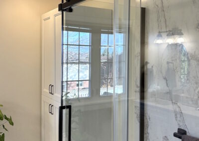 A custom bathroom from Peterborough Bath Renovators with a glass shower sliding door, with a black frame and handle.